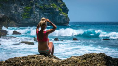Kayanın üzerinde oturan ve büyük Tembeling kıyı şeridi Nusa Penida Island, Bali Endonezya isabet dalgaları seyretmekten kız