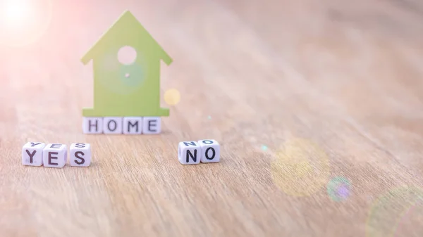 HOME YES NO horizontal word of cube letters with green house symbol on wooden surface