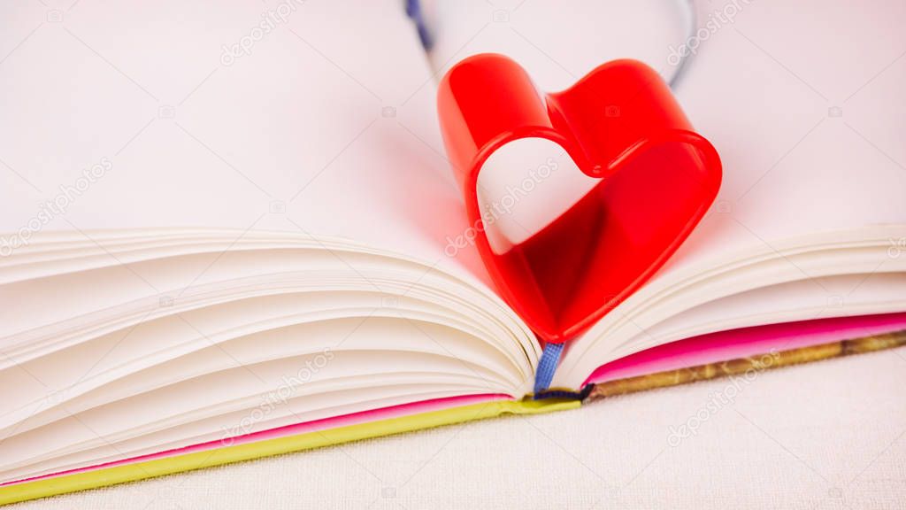 Red heart over diary book on white table