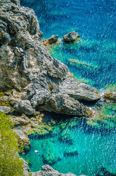 Touristen zwischen Felsen in der azurblauen Bucht von Paleokastritsa auf der griechischen Insel Korfu — Stockfoto