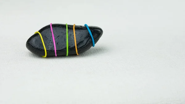 Sendo diferente uma pedra preta com listras coloridas em fundo brilhante — Fotografia de Stock