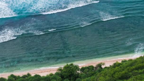 Ovanifrån perspektiv av vågorna som rullar en i taget till den Nunggalan Beach, Uluwatu, Bali, Indonesien — Stockvideo