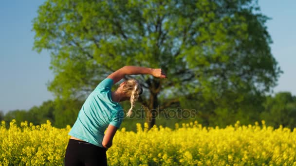 Fitness training of an gild at open air. Blooming fresh yellow rapeseed field with an big oak tree in background — Stock Video