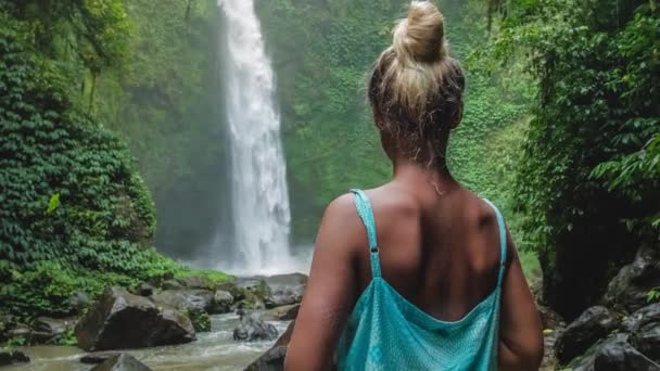 Frauen vor tropischen Wasserfällen, umgeben von sattgrünem Dschungel. Fallendes Wasser trifft die Wasseroberfläche. leichte Brise — Stockvideo