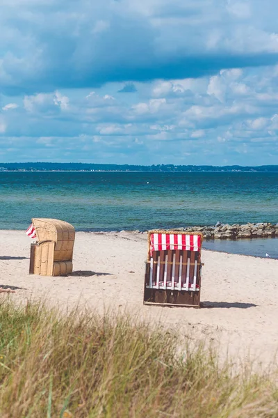 Red striped roofed chairs on empty sandy beach in Travemunde. Grass bush in foreground. Germany — Stock Photo, Image