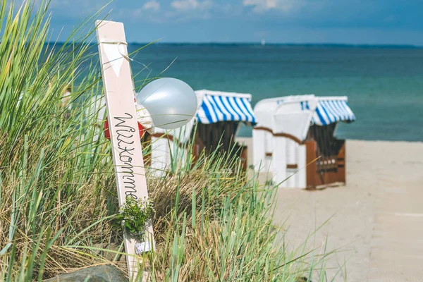 Blå farvede tagstole på sandstrand i Travemunde, Velkommen balloner. Tyskland - Stock-foto