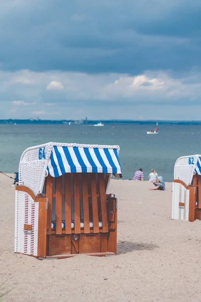 Cadeiras de telhado listradas azuis na praia de areia vazia em Travemunde. Pessoas desfocadas no fundo — Fotografia de Stock