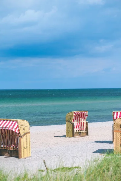 Κόκκινο ριγέ στεγασμένη καρέκλες σε άδειο αμμώδη παραλία στο Travemunde. Θάμνο χλόης σε πρώτο πλάνο. Γερμανία — Φωτογραφία Αρχείου