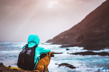 Dağlar ve dalgalar ve Bulutların arasından gelen güneş ışınları ile kırsal kıyı şeridi manzara önünde bir köpek olan adam. Santo Antao Adası, Cape Verde