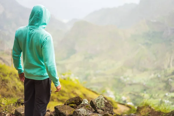 Tourist in hoodie in front of rural landscape with mountains, on the way of the Paul Valley. Santo Antao Island, Cape Verde