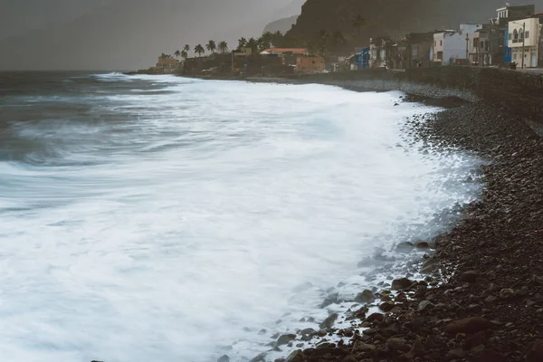 Lange blootstelling de golven van de oceaan van het schuim met blazen spray op vulkanische rotsenstranden. Woningen aan Ribeira Grande op een stormachtige dag — Stockfoto