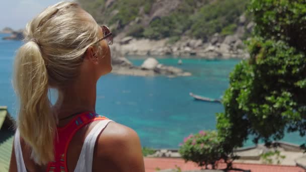 Mujer deportiva bronceada disfrutar de magníficas vistas de la bahía de Tanote en el día soleado. Ligera brisa del océano brisa del océano tamizada a través de su cabello rubio. Koh Tao, Tailandia — Vídeos de Stock