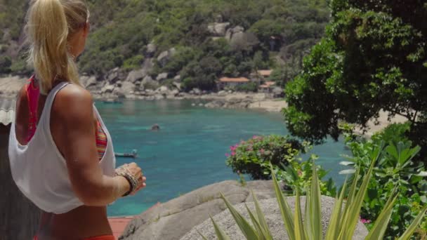 Mujer deportiva bronceada disfrutar de magníficas vistas de la bahía de Tanote en el día soleado. Ligera brisa del océano brisa del océano tamizada a través de su cabello rubio. Koh Tao, Tailandia — Vídeos de Stock