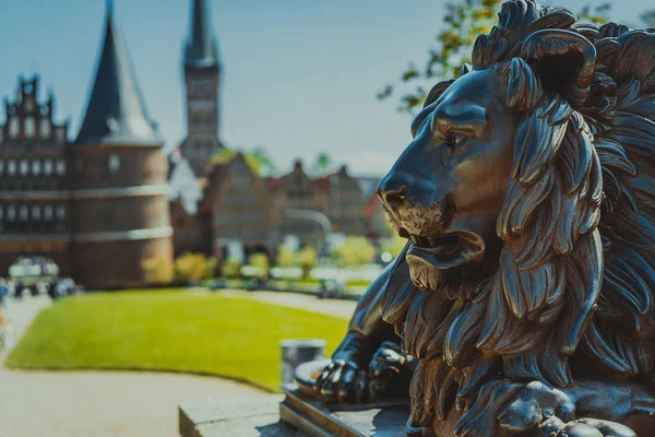 Bronze Lion statue in front of Holsten Gate - Holstentor, a city gate marking off the western boundary of the old center of Luebeck in Schleswig-Holstein, northern Germany