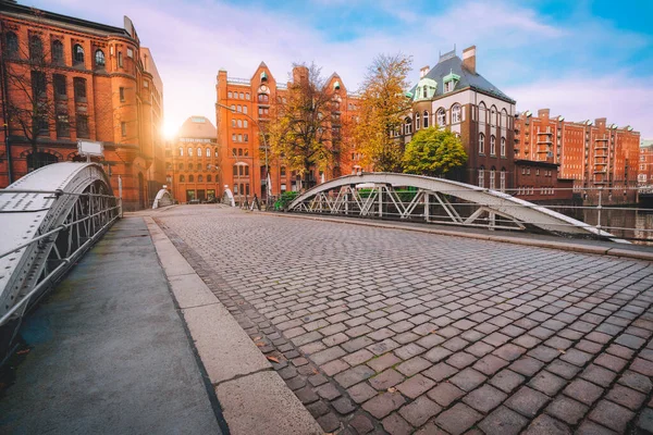 Bågbro över kanaler med kullerstensväg i Speicherstadt i Hamburg, Tyskland, Europa. Historisk röd tegelbyggnad upplyst av gyllene solnedgång ljus nära vatten slott palats — Stockfoto