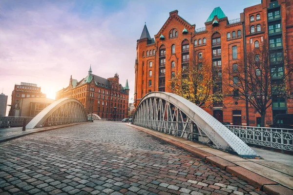 stock image Arch bridge over alster canals with cobbled road in historical Speicherstadt of Hamburg, Germany, Europe. Scenic view of red brick building lit by golden sunset light