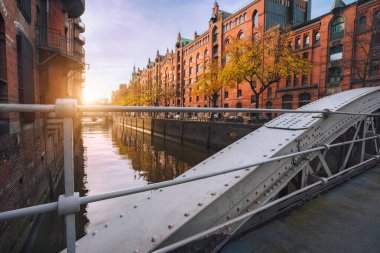 Hamburg, Almanya ve Avrupa 'daki Speicherstadt kanallarında kemer köprüsü. Tarihsel kırmızı tuğla bina sıcak, yumuşak, altın gün batımı ışığıyla aydınlanıyor.
