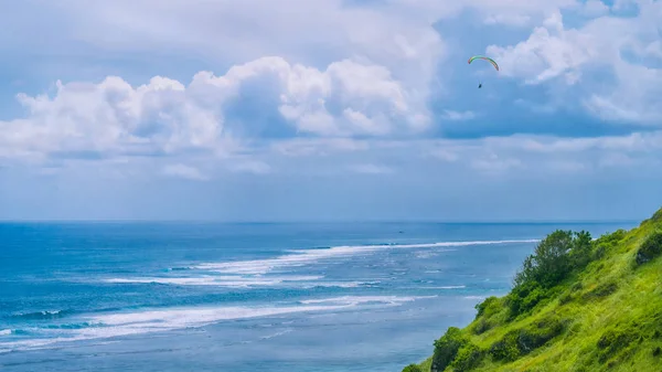 Paraglider flyger de gräsbevuxna kullarna ovanför Gunung Payung strand i nordöstra Bali en av de populära områdena för skärmflygning — Stockfoto