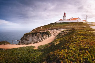 Portekiz Sintra bölgesine git. Cabo da Roca 'daki ya da Cape Roca' daki güneş ışığı ve alçak bulutlardaki deniz fenerinin görüntüsü