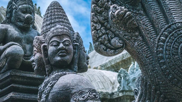 Skulptur van wilde mensen met veel bizarre gezichten. Oude stenen tempel op de achtergrond — Stockfoto