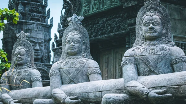 Skulptur of wild people with bizarre faces. Ancient temple with stone face in background — Stock Photo, Image