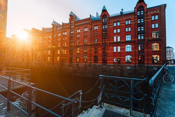 Um tijolo vermelho casas de vários andares de Speicherstadt Hamburgo. Famoso marco de velhos edifícios de tijolos vermelhos em luz dourada do pôr do sol. Vista panorâmica da noite com corrimão do canal em primeiro plano — Fotografia de Stock