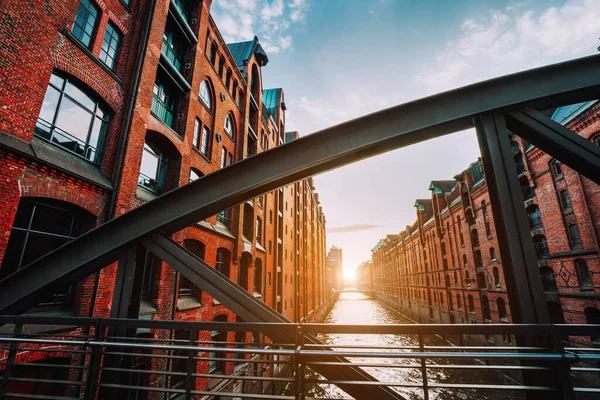 O armazém de tijolos vermelhos - distrito de Speicherstadt, em Hamburgo, Alemanha, emoldurado por vigas de arco de ponte de aço com perspectiva de canal preenchida por luz quente do pôr do sol — Fotografia de Stock