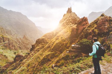 Santo Antao Adası, Cape Verde. Gün batımında kameralı bir gezgin dağ sırtının önünde ve Xo-Xo Vadisi 'ne giden kaldırımlı yolda.