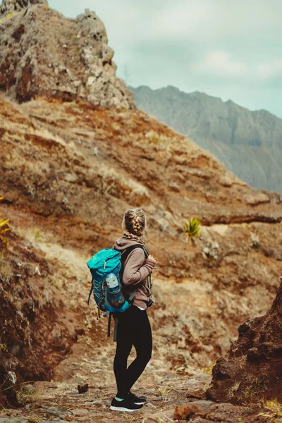 Ilha de Santo Antão, Cabo Verde. Caminhante feminina com mochila azul permanecendo na rota pedregosa de trekking com terreno árido ao redor — Fotografia de Stock