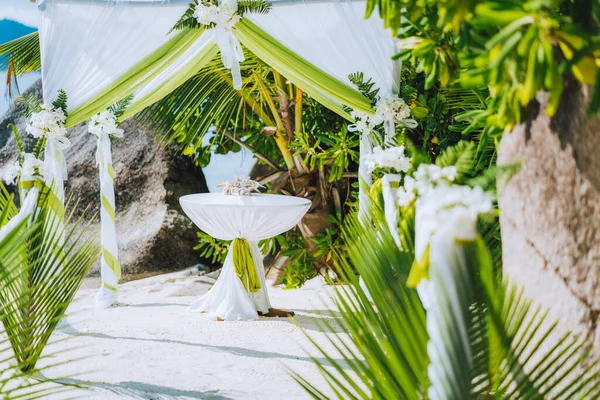 Decorated romantic wedding celebration location, table and chairs on tropical beach. Lush green foliage and white lowers — Stock Photo, Image