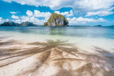 Tropik plajlarda avuçiçi gölgeleri Las Cabanas. Arka planda benzersiz bir tropikal ada var. El Nido, Palawan, Filipinler 'deki güzel manzara