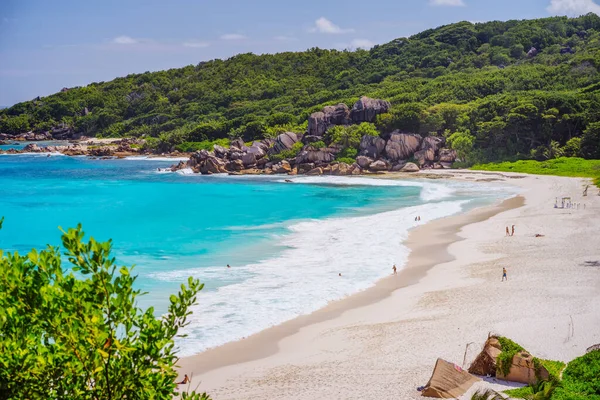 Grand Anse strand La Digue sziget Seychelles. Hosszú fehér homokos strand kék lagúna, óceán hullámok és gránit sziklák a háttérben — Stock Fotó