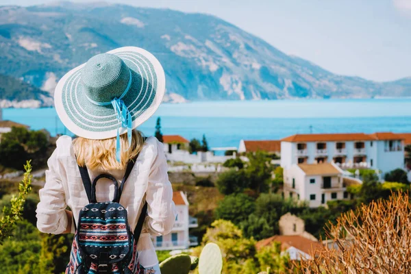 Mulher turística com chapéu de sol azul desfrutando grego bonito e colorido Assos cidade na ilha de Kefalonia, Grécia — Fotografia de Stock