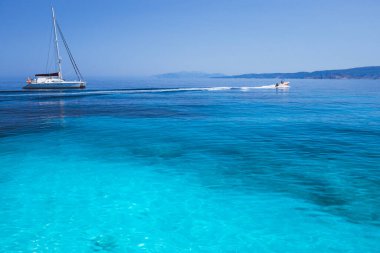 Tatil tatili. Sakin dalgaları olan mavi göl ve arka planda kıyı şeridi olan katamaran yelkenli yat.