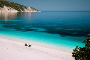 Fteri plajı, Kefalonia, Yunanistan. Yaz tatili. Güneş şemsiyesinden saklanan tanınmayan yalnız turist çifti berrak mavi zümrüt deniz suyu gölünün yanında rahatla.