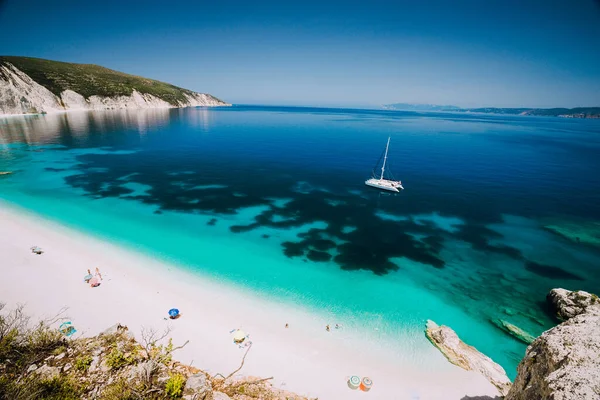 Weiße Katamaranjacht in klarem, blauem Meerwasser. Touristen am Sandstrand in der Nähe der azurblauen Lagune. Kefalonia, Griechenland — Stockfoto