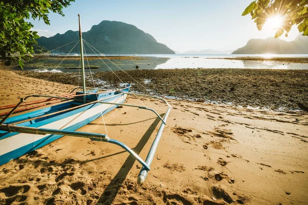 Bateau Bangka sur une plage de sable avec coucher de soleil doré sur des îles tropicales en arrière-plan. Baie d'El Nido. Philippines — Photo