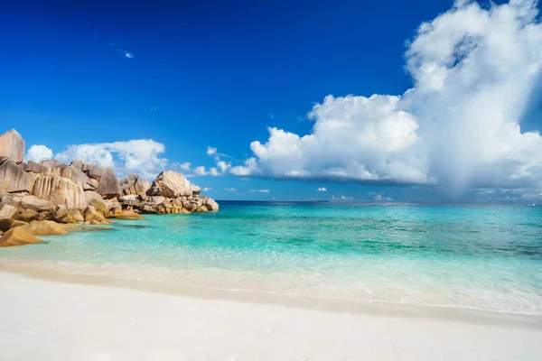 Luminosa giornata di sole a Grand Anse spiaggia a La Digue isola alle Seychelles. Spiaggia di sabbia con baia blu oceano, nuvole bianche sullo sfondo — Foto Stock