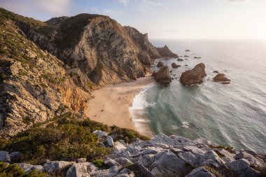 Praia da Ursa Sahili, gün batımında, Sintra, Portekiz 'de. Kumsalın manzarası, deniz yığını kayalar ve altın ışıkla aydınlatılmış okyanus dalgaları. Atlantik Okyanusu 'nun gerçeküstü kıyıları