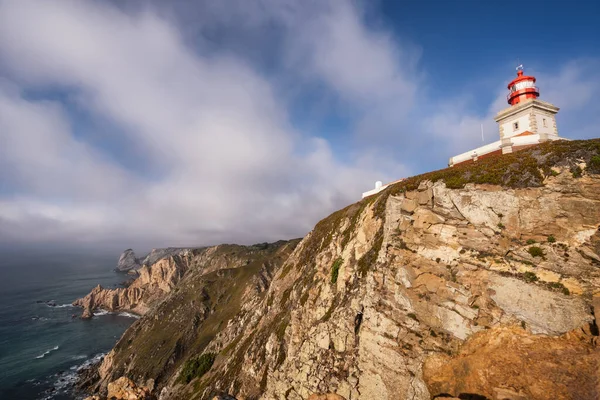 카보 다 로카 등대 (Cabo da Roca Lighthouse) 는 저녁 햇살 이 아름다운 구름을 막아 주는 절벽 가장자리에 있다. 유럽 대륙에서 가장 서쪽에 위치 한 시트라, 포르투갈. 휴일 여행 목적지 — 스톡 사진