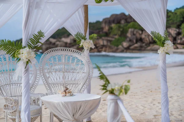 La Digue, Seychelles. Wedding arch gazebo ceremonial decorated with white flowers on a tropical grand anse sand beach. Famous granite stones in background — Stock Photo, Image