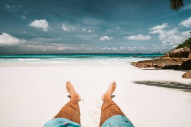Tropik tatil. Adam kumlu bir plajda uzanıyor ve eğleniyor. Okyanus ve mavi gökyüzünde.