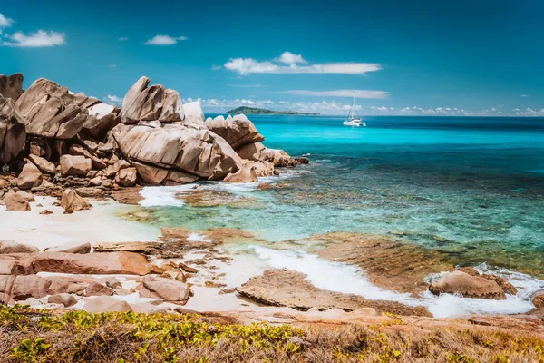 Grand L Anse, La Digue, Seychelles. Trópusi tengerpart rejtett stranddal, egyedi gránit sziklákkal és magányos vitorlás hajóval a kék óceánon — Stock Fotó