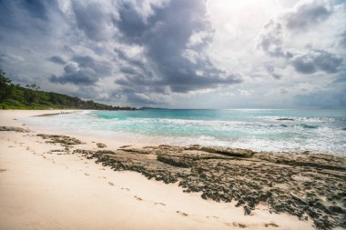 Grand Anse plajı, Seyşeller, La Digue, tropikal kumlu plaj, mavi okyanus ve yağmurlu bulutlar.