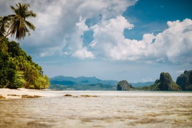 El Nido, Palawan, Filipinler. Sığ göl manzarası, palmiye ağaçlı kumlu plaj. Arka planda egzotik adalar ve beyaz bulutlar