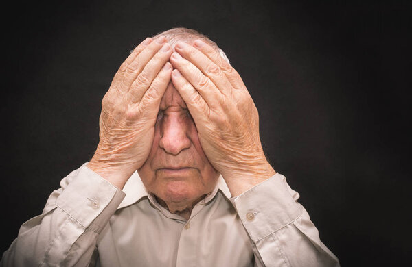 Портрет пожилого человека с закрытым руками лицом
