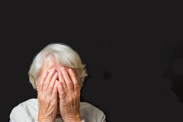 Ritratto di una donna anziana con il volto chiuso dalle mani sul nero — Foto Stock