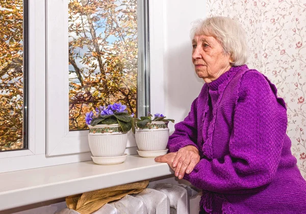Velha mulher solitária sentada perto da janela em sua casa. — Fotografia de Stock
