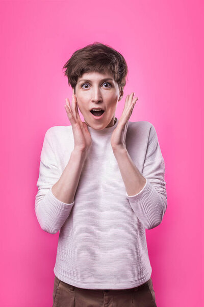 Beautiful female half-length portrait over pink studio backgroud. The young emotional smiling and surprised woman standing and looking at camera.