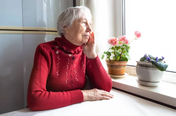 Vieja mujer solitaria sentada cerca de la ventana de su casa. — Foto de Stock